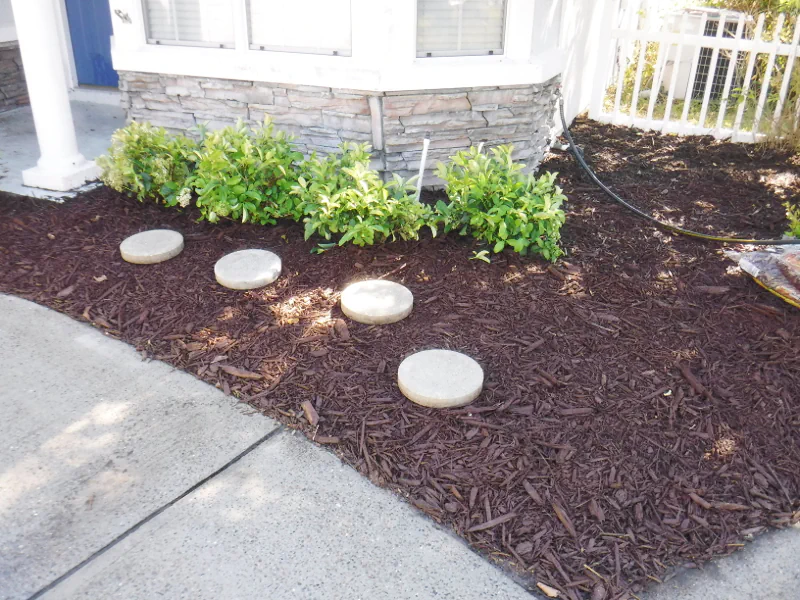 brown mulch in small flower bed with white steppingstones