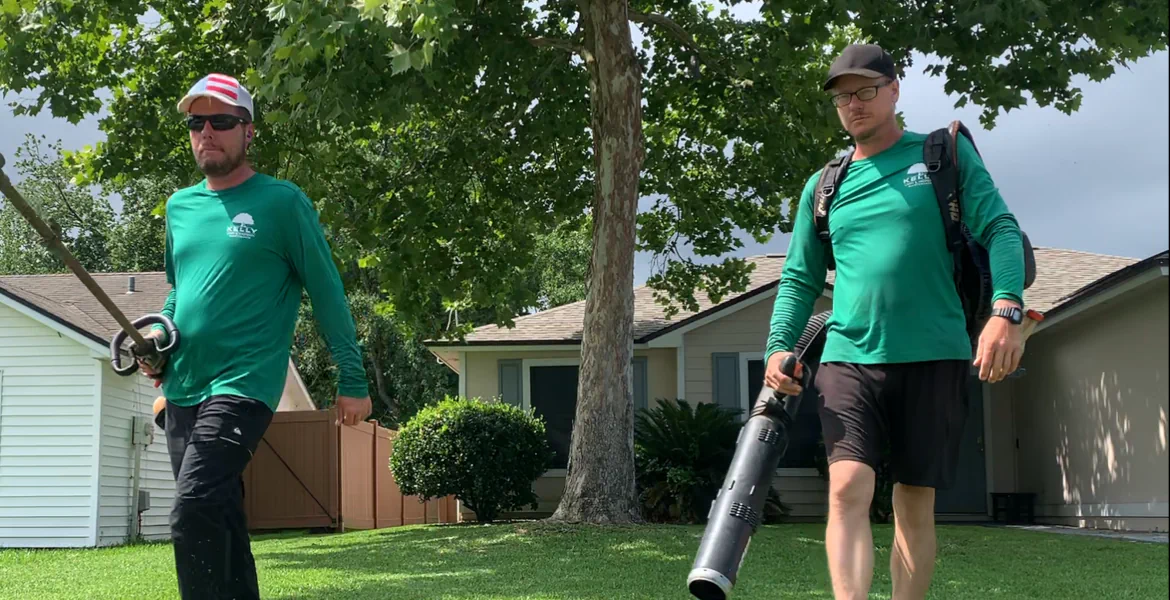 company owners on a customer's lawn. one person has a string trimmer and the other has a backpack blower